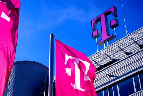 Graues Telekom Gebäude mit Logo auf dem Dach und Telekom Fahnen vor dem Eingang