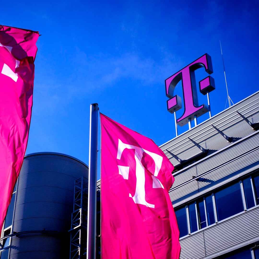 Graues Telekom Gebäude mit Logo auf dem Dach und Telekom Fahnen vor dem Eingang