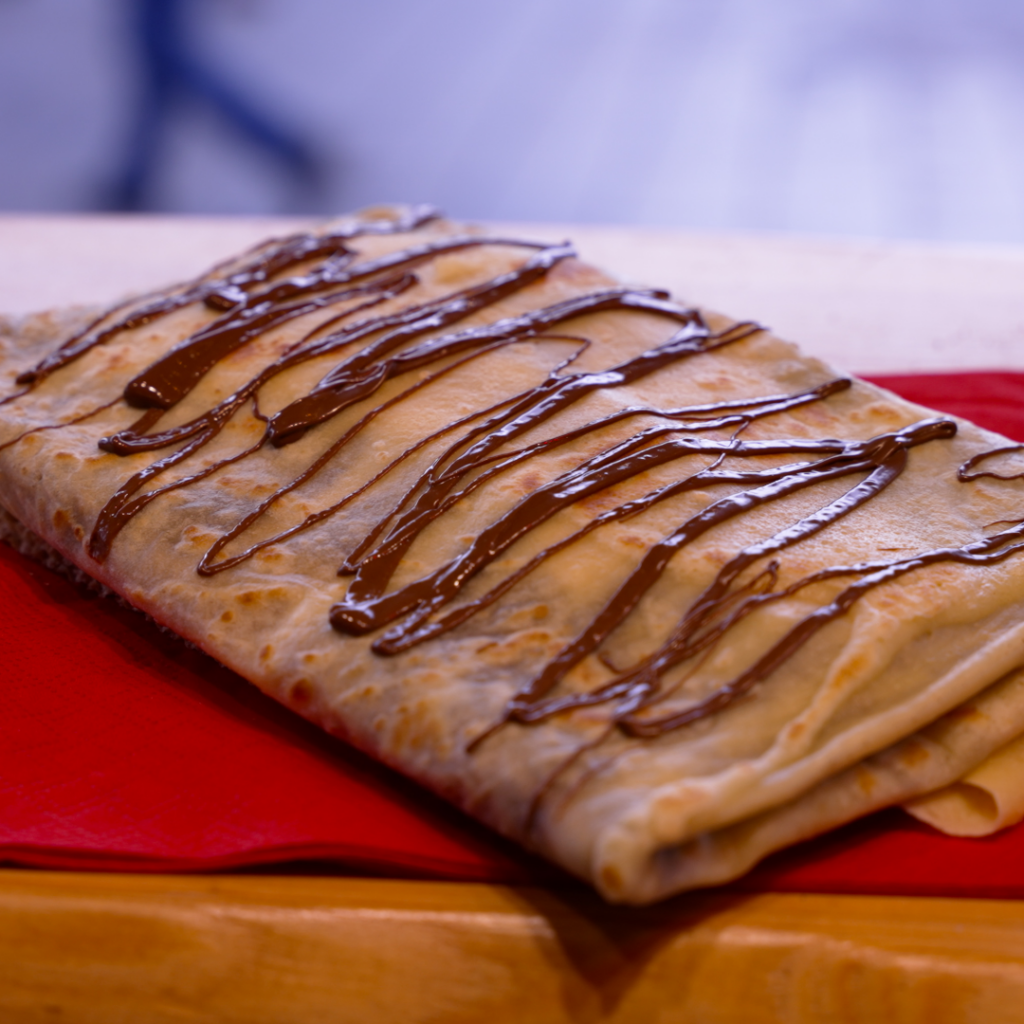 Crepe mit Nutella auf einem roten Tuch serviert, fotografiert auf einem Holztisch