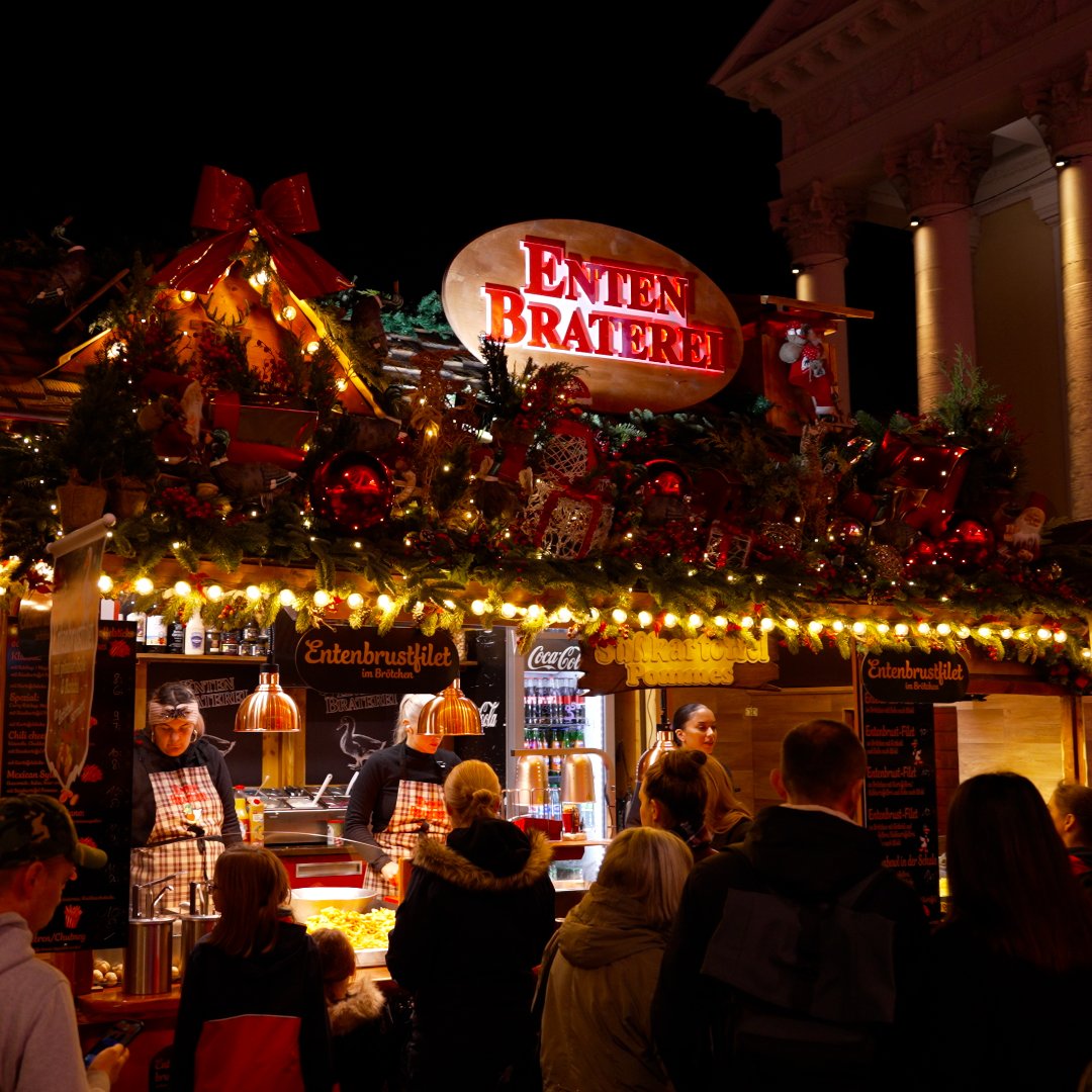 Entenbraterei auf dem Karlsruher Weihnachtsmarkt am Abend mit Besuchern vor dem Stand